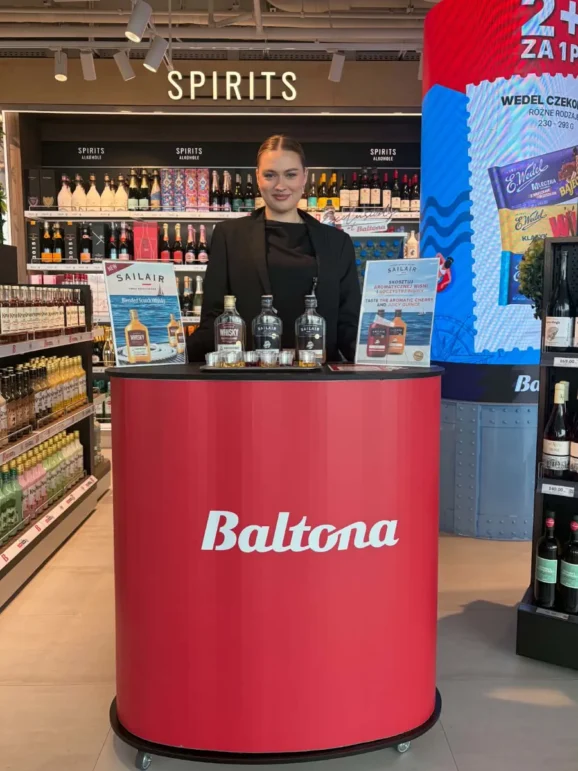 Hostessa prezentująca ofertę i zapraszająca podróżnych do degustacji w sklepie lotniskowym Baltona